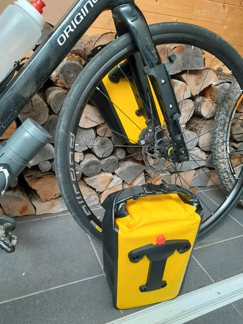 Support vissé sur les œillets de la fourche et sacoche jaune posée au sol, fixation en T visible