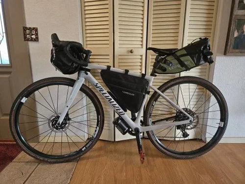 Vélo gravel équipé d'une sacoche de guidon étanche, d'une sacoche de cadre et d'une sacoche de selle