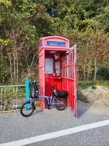 Vélo pliant chargé d'un sac étanche pour un voyage de trois jours, garé devant une cabine rouge