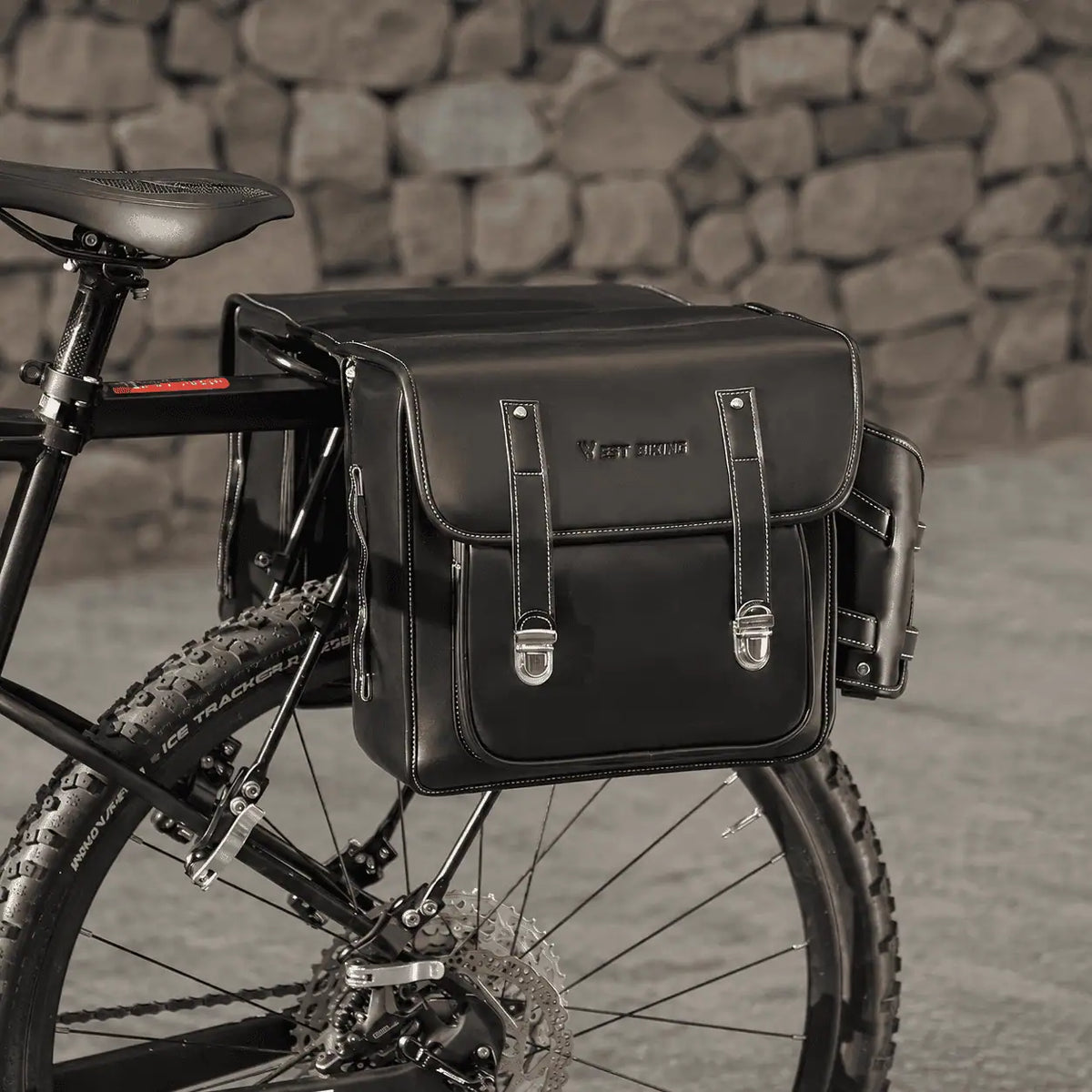 Double sacoche noire en cuir fixee sur le porte-bagage arriere d'un VTT.