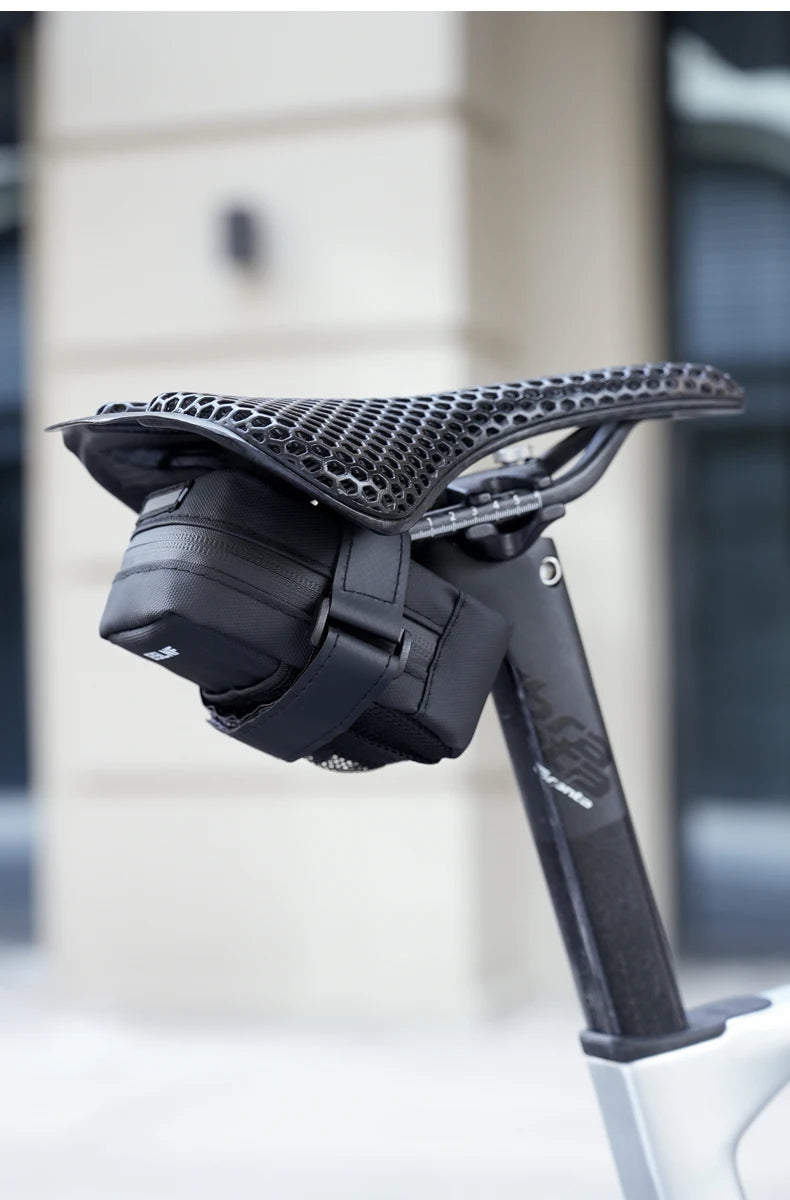 Petite sacoche de selle vélo noire sous une selle ajourée, vue arrière de trois quarts