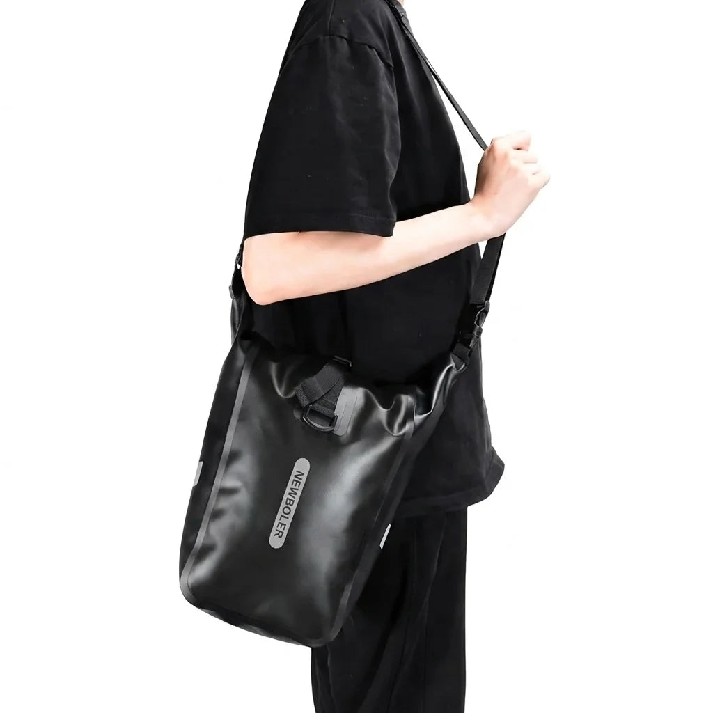 Personne portant un sac etanche noir en bandouliere sur l epaule, presente sur fond blanc.
