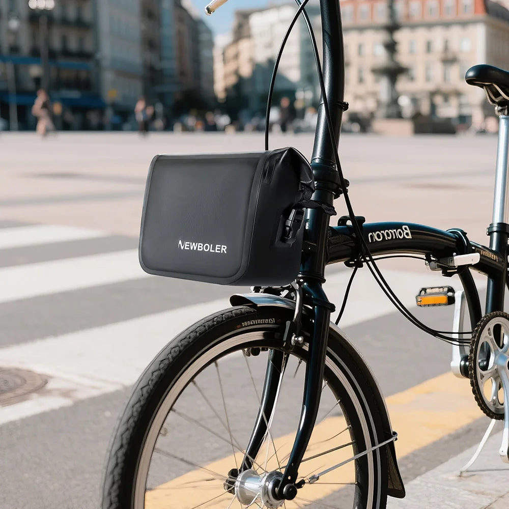 Sacoche de cadre noire installee sur un velo pliant noir gare en ville, avec une place et des immeubles en arriere-plan.