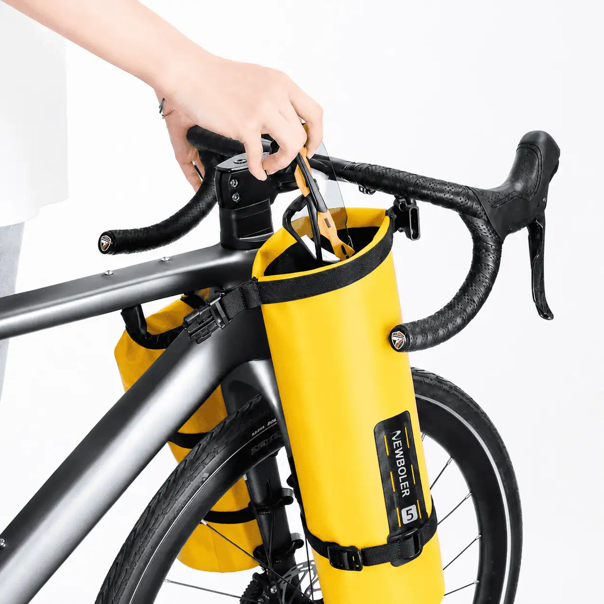 Main ouvrant une sacoche de fourche jaune 5L fixee sur la fourche d'un velo de route argente.