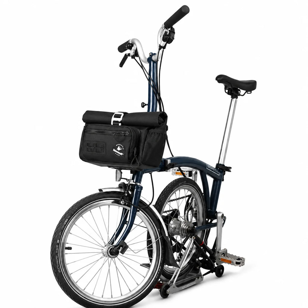 Sacoche de guidon noire fixée à l'avant d'un vélo pliant bleu marine, vue de côté sur fond blanc.