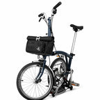 Sacoche de guidon noire fixée à l'avant d'un vélo pliant bleu marine, vue de côté sur fond blanc.