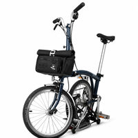 Sacoche de guidon noire fixée à l'avant d'un vélo pliant bleu marine, vue de côté sur fond blanc.
