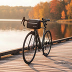 Vélo de route gris avec sacoche de guidon noire posé sur un ponton en bois au bord d'un lac en automne