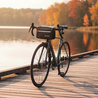 Vélo de route gris avec sacoche de guidon noire posé sur un ponton en bois au bord d'un lac en automne