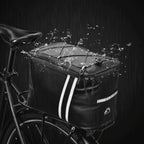 Sacoche de porte-bagage vélo noire installée sur un vélo sous la pluie, avec des éclaboussures d'eau illustrant son imperméabilité.