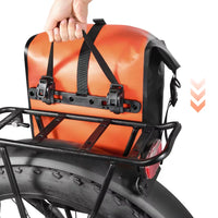 Main soulevant une sacoche de porte-bagage orange fixée sur un porte-bagage de vélo fat bike