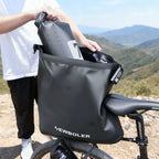 Personne ouvrant une grande sacoche de selle noire impermeable fixee sous la selle d'un velo, en pleine nature.