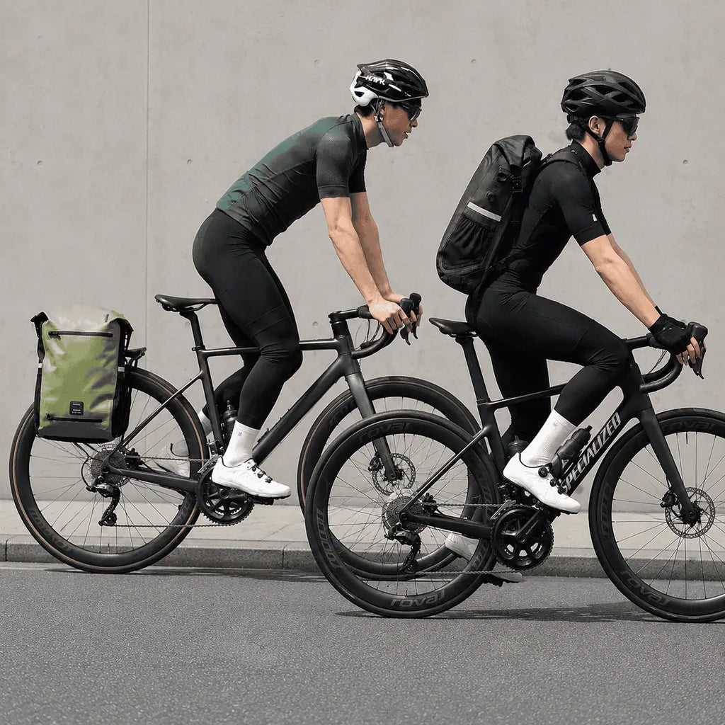 Deux cyclistes sur route, le modèle vert fixé au porte-bagages et le modèle noir porté sur le dos