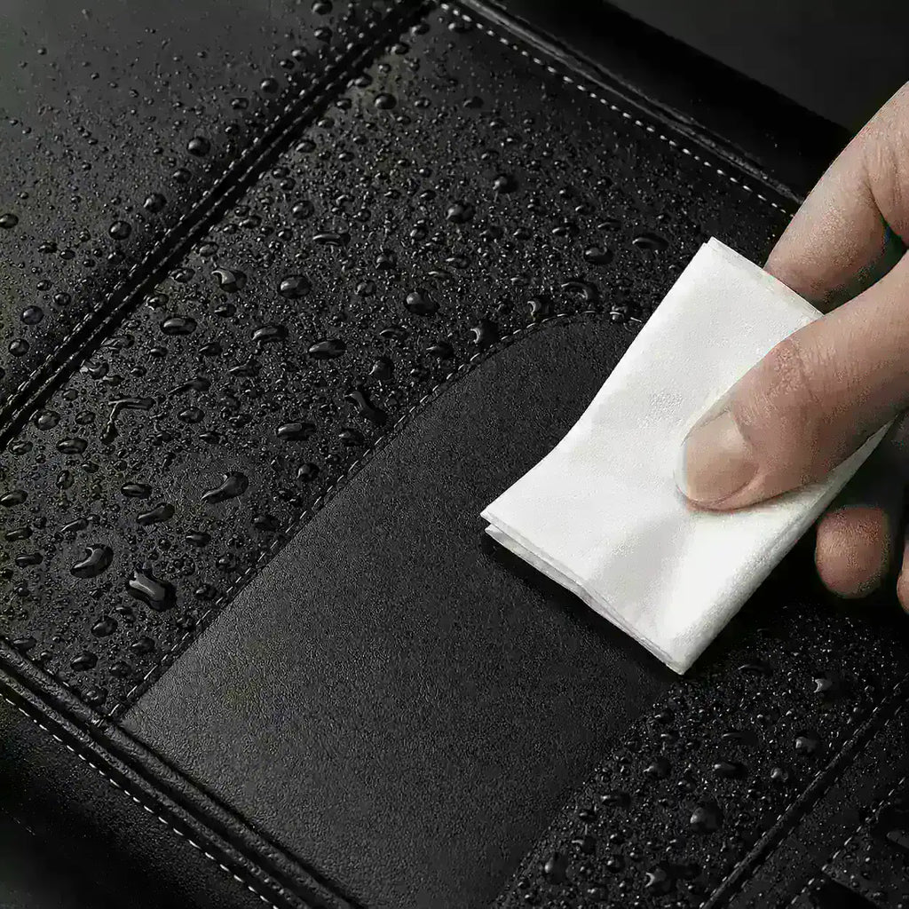 Main essuyant une sacoche de velo noire couverte de gouttelettes d'eau avec un chiffon.
