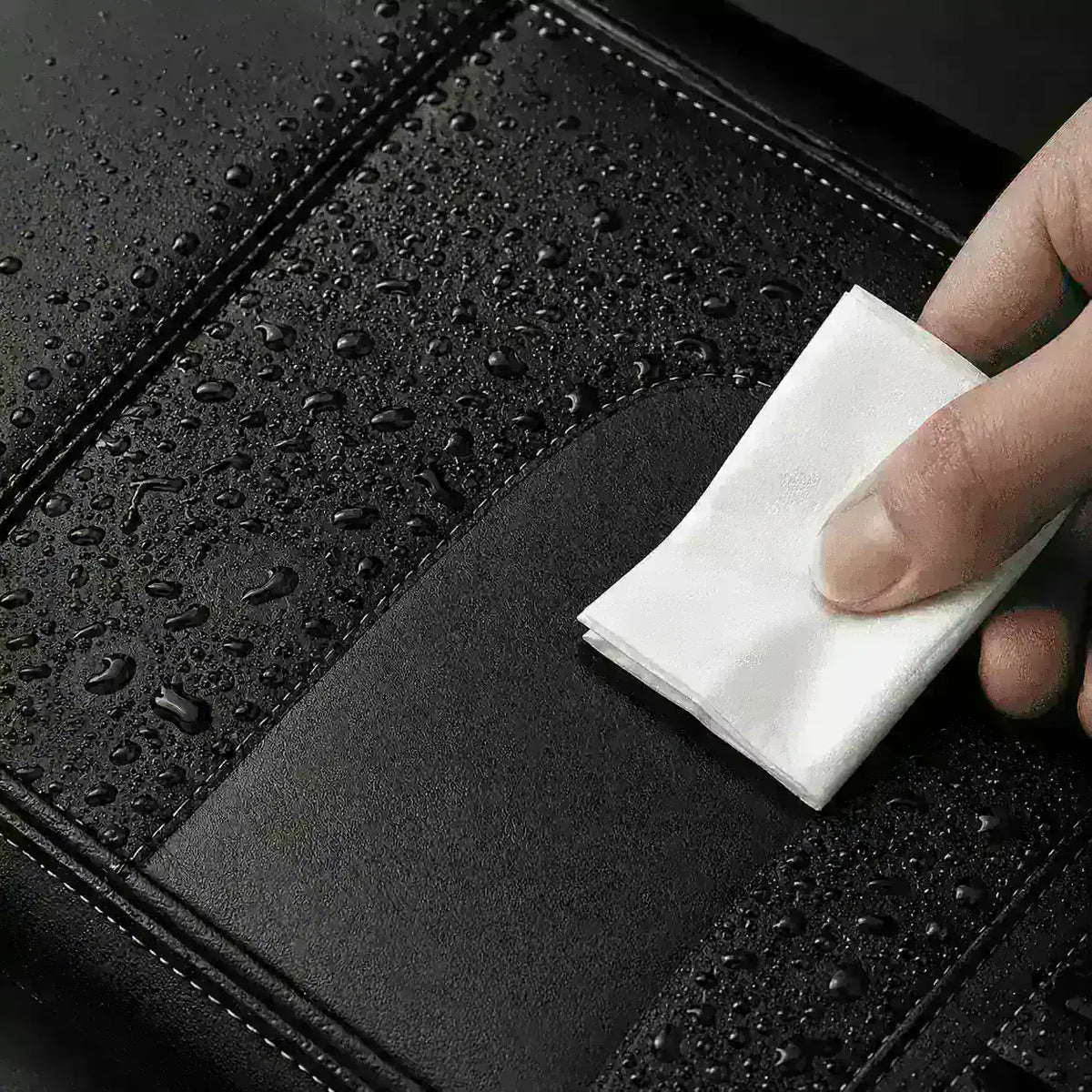 Main essuyant une sacoche de velo noire couverte de gouttelettes d'eau avec un chiffon.