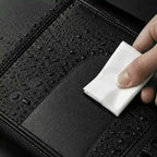 Main essuyant une sacoche de velo noire couverte de gouttelettes d'eau avec un chiffon.
