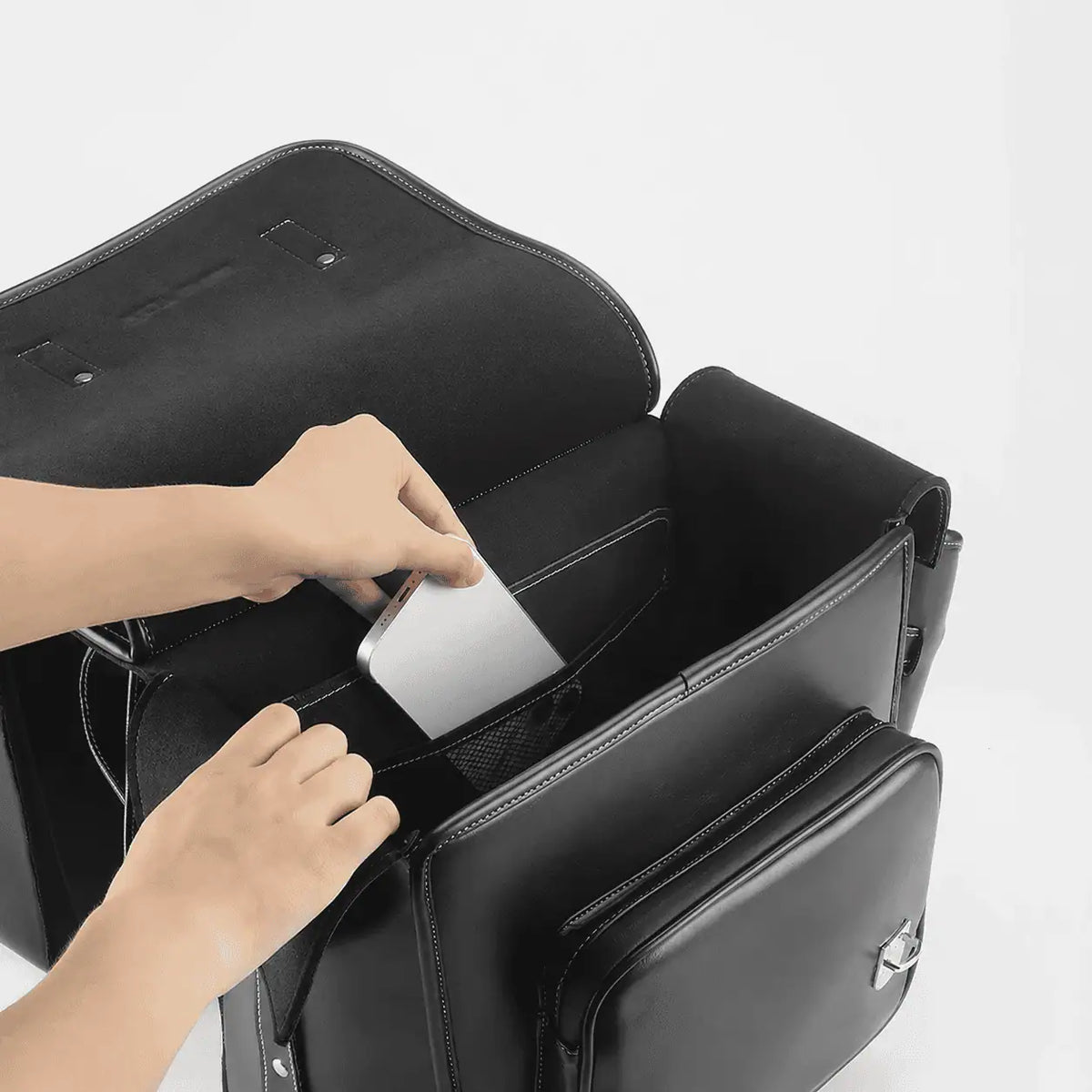 Mains inserant un ordinateur portable dans une sacoche de velo noire ouverte sur fond blanc.