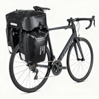 Deux sacoches laterales noires volumineuses fixees sur le porte-bagage arriere d'un velo de route noir.