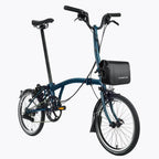 Velo pliant bleu avec sacoche de cadre noire installee, presente de profil sur fond blanc.