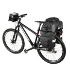 Velo VTT noir equipe d'un set de sacoches noires sur le porte-bagages arriere et d'une sacoche de guidon.