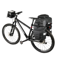 Velo VTT noir equipe d'un set de sacoches noires sur le porte-bagages arriere et d'une sacoche de guidon.